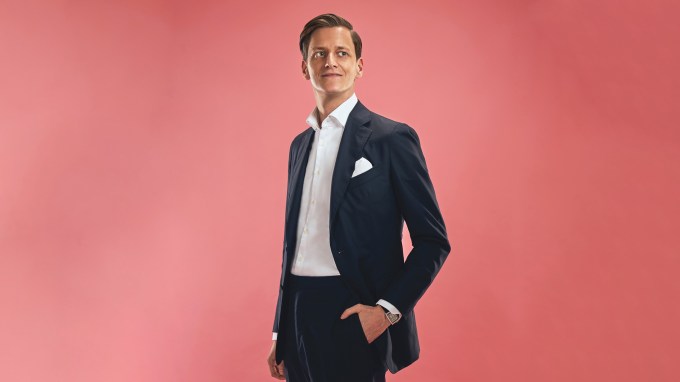 Portrait of etaily founder Alexander Friedhoff wearing a black suit and white shirt against a rose colored background