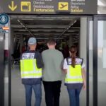 a photo of the back of two police officers leading an alleged hacking suspect into an airport