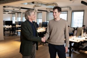 French CEO of AFP (Agence France Presse) Fabrice Fries (L) shakes hands with French founder of artificial intelligence start-up Mistral AI, Arthur Mensch at the Mistral headquarters in Paris, on January 15, 2025. AFP (Agence France-Presse) and Mistral have signed an agreement that allows the conversational robot of the French start-up that aims to become Europe's leading AI player to use the agency's news dispatches to answer its users' queries, they announced on January 16, 2025.