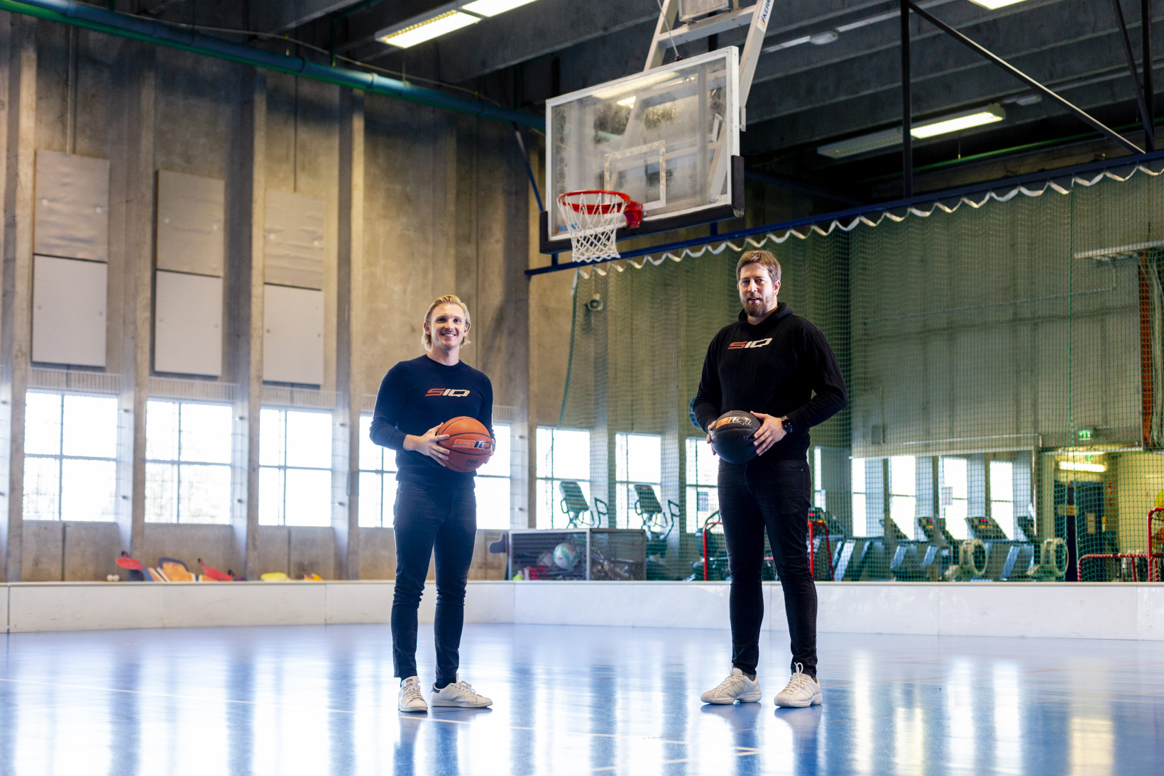 Erik Anderson (left), CEO of SportIQ, and Harri Hohteri, founder of SportIQ, holding basketballs under a basketball net