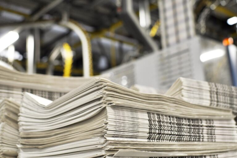 stack of freshly printed daily newspapers transported to a printing plant, in the background machines and technical equipment of a large printing plant